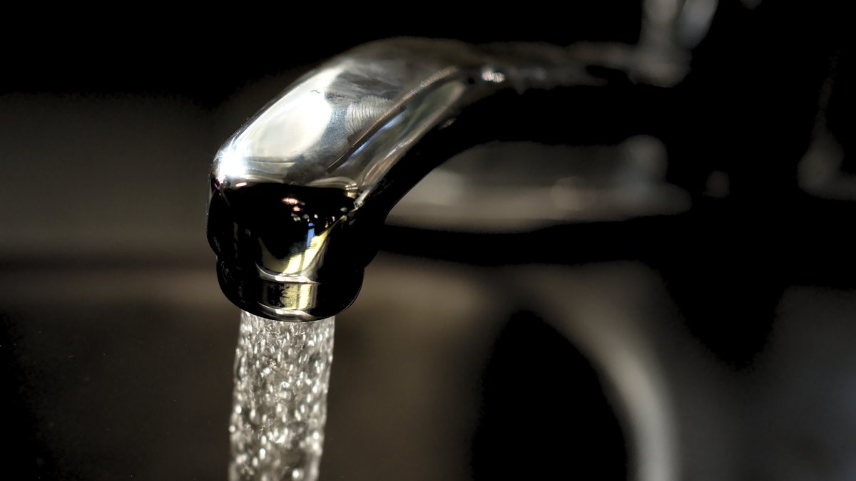 Close-up of a chrome kitchen faucet with a stream of tap water running from the spout